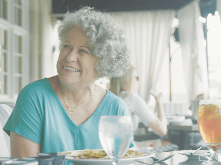 Image of a happy woman sitting at a table eating a meal